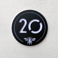 Manchester Bee House Sign in matt black mounted on a rendered exterior wall, shown at an angle