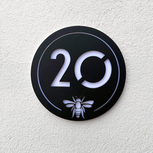 Manchester Bee House Sign in matt black mounted on a rendered exterior wall, shown at an angle