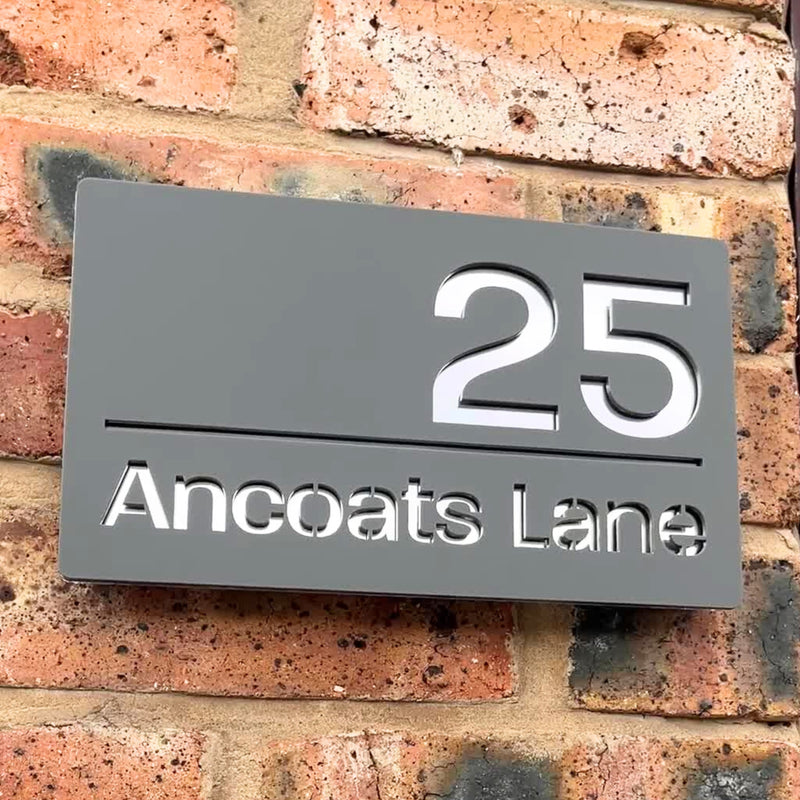 Matt grey modern house sign installed on a rendered wall